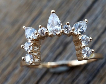May include: A gold ring with a delicate design featuring a row of pear-shaped and round clear gemstones.