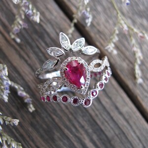 May include: Three silver rings with a pear-shaped ruby gemstone surrounded by smaller diamonds. The top ring features a floral design with five diamond leaves. The middle ring has a delicate, intricate design with diamonds. The bottom ring has a row of small ruby gemstones.