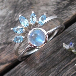 Conjunto de dos anillos nupciales con halo de piedra lunar y aguamarina: anillo de compromiso redondo de piedra lunar azul con alianza de aguamarina en oro blanco.
