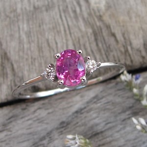 May include: A delicate silver ring with a pink oval gemstone and two smaller diamond accents.