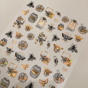 May include: Gold and black bee-themed nail stickers with various designs including bees, honey pots, honeycombs, flowers, and the text "Bee Honey" and "Bee Happy".