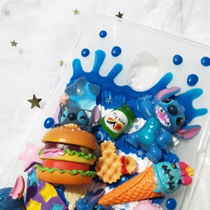 Op de afbeelding: Een transparante telefoonhoes met een blauw en wit ontwerp met een cartoonfiguur, Stitch, uit de Disney-film Lilo & Stitch. De hoes bevat ook een hamburger, een ijsje en een wafel.