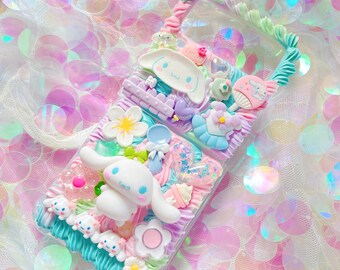 Può includere: Una custodia per telefono trasparente decorata con decorazioni 3D color pastello, tra cui un cane bianco dei cartoni animati, fiori e un cucchiaio. La custodia ha un design a spirale blu chiaro, verde e rosa e il testo "Welcome" è visibile in alto.