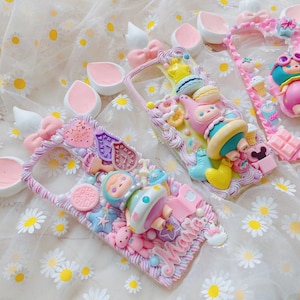 May include: Three decorative phone cases with whimsical designs. Each case features a unique arrangement of colorful, sculpted elements, including bows, stars, and cartoon characters. The cases are in shades of pink, blue, and yellow, with a textured, decorative border.