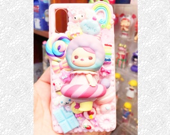 Puede incluir: Una funda de teléfono rosa con un diseño 3D de caramelos y personajes. La funda presenta un personaje rosa y blanco con un bastón de caramelo y una piruleta. El texto "Angie" está en la funda.