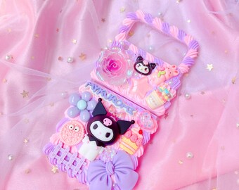 Può includere: Una custodia per telefono rosa e viola con un design 3D che presenta un personaggio dei cartoni animati in bianco e nero, una rosa rosa e altri elementi decorativi. La custodia ha un retro trasparente e un bordo rialzato attorno ai bordi.