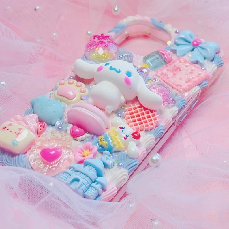Pu&ograve; includere: Una custodia per telefono bianca decorata con decorazioni 3D color pastello, tra cui un cane bianco dei cartoni animati, un cuore rosa, un castello blu e un waffle rosa e bianco. La custodia &egrave; ricoperta di glitter e strass.