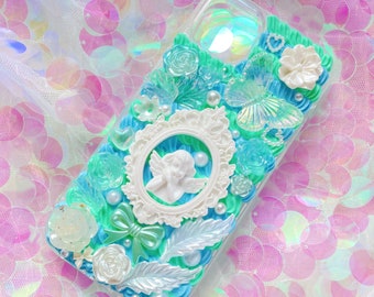 Può includere: Una custodia per telefono trasparente decorata con un cherubino bianco, fiori blu e verdi, una farfalla e perle.