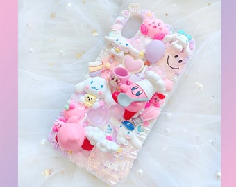 May include: A pink and white phone case decorated with various charms, including a pink and white character with a chef's hat, a pink and white character with a spoon, a pink and white character with a cloud, and a pink and white character with a heart. The case also features a pink and white smiley face, a pink and white heart, and a pink and white star.