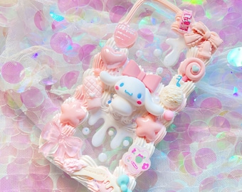 Può includere: Una custodia per telefono trasparente decorata con decorazioni 3D rosa, bianche e blu. La custodia presenta un cane di cartone animato bianco con un fiocco rosa, una stella rosa, un vortice rosa e un lecca-lecca rosa. La custodia è su uno sfondo rosa e bianco.