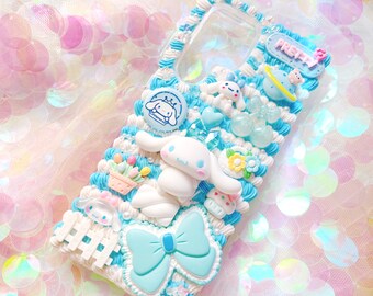 Può includere: Una custodia per telefono bianca decorata con decorazioni 3D blu e bianche, tra cui un grande fiocco blu, una piccola figurina di cane bianco e un piccolo fiore bianco. La custodia presenta anche un piccolo cartello blu e bianco che dice "PRETTY".