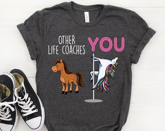 May include: Dark gray t-shirt with the text "Other Life Coaches" and a brown horse on the left side. On the right side, the text "You" is in pink and a unicorn is doing a pole dance.