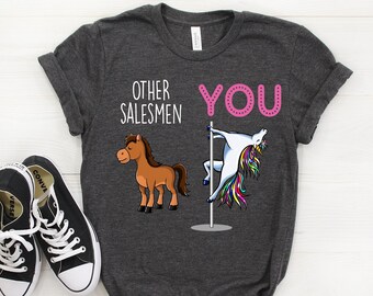 May include: A dark gray t-shirt with the text "Other Salesmen" and a cartoon horse on the left side. On the right side, the text "You" is in pink and a cartoon unicorn is doing a pole dance.