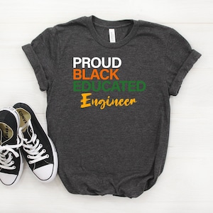 May include: A dark grey t-shirt with the text "PROUD BLACK EDUCATED Engineer" in white, black, green, and orange lettering.