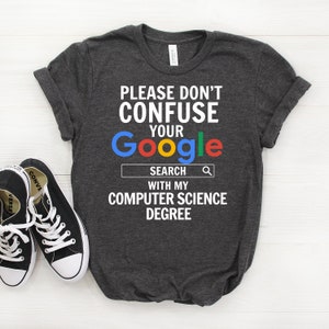 May include: Dark grey t-shirt with the text "PLEASE DON'T CONFUSE YOUR Google SEARCH WITH MY COMPUTER SCIENCE DEGREE" in white. The word "Google" is in the Google logo colours.