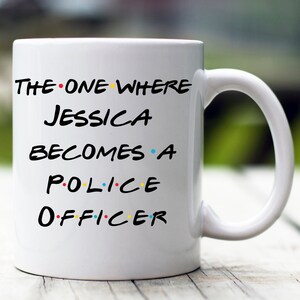 May include: White ceramic mug with black text that reads "The One Where Jessica Becomes a Police Officer" with colorful dots between each word.