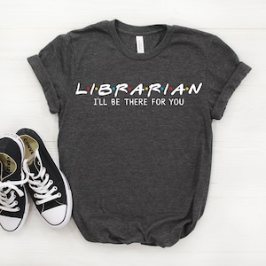 May include: A dark heather grey t-shirt with the text "LIBRARIAN I'LL BE THERE FOR YOU" in white. The text is styled like the Friends logo.