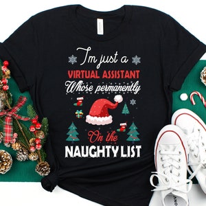 May include: Black t-shirt with the text "I'm just a Virtual Assistant Whose permanently On the Naughty List" in white and red. The design includes a Santa hat, Christmas trees, and snowflakes. A festive holiday tee.