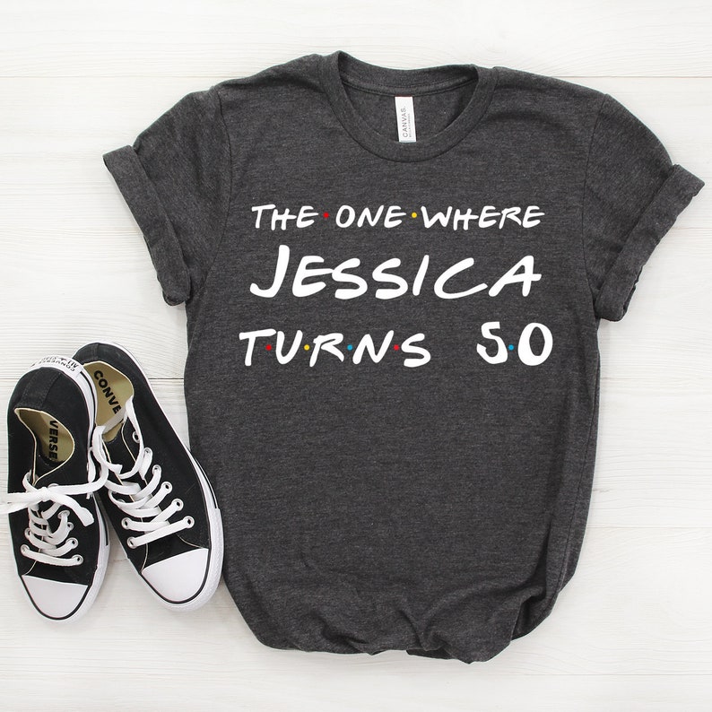 May include: A dark gray t-shirt with the text "The One Where Jessica Turns 50" in white. The text is styled to look like the title card from the TV show Friends.