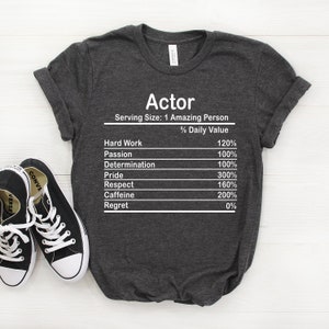 May include: A dark grey t-shirt with the word "Actor" printed on the front. The shirt has a nutrition facts label with the following information: Serving Size: 1 Amazing Person, Hard Work 120%, Passion 100%, Determination 100%, Pride 300%, Respect 160%, Caffeine 200%, Regret 0%.