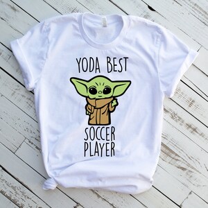 May include: White t-shirt with a green cartoon character and the text "Yoda Best Soccer Player".