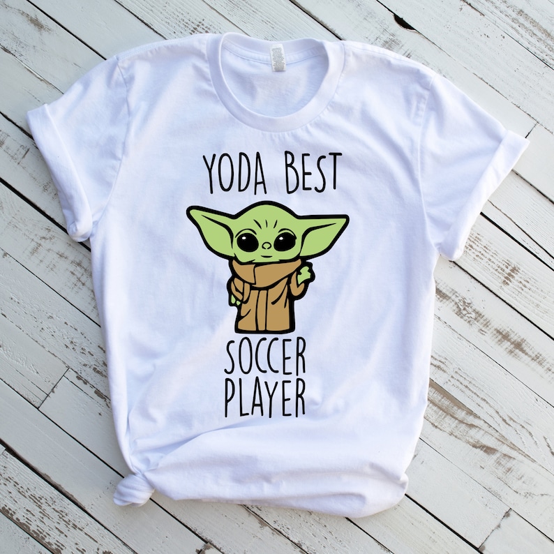 May include: White t-shirt with a green cartoon character and the text "Yoda Best Soccer Player".