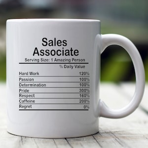May include: White ceramic mug with a black graphic that reads "Sales Associate" and lists the daily value percentage of hard work, passion, determination, pride, respect, caffeine, and regret.
