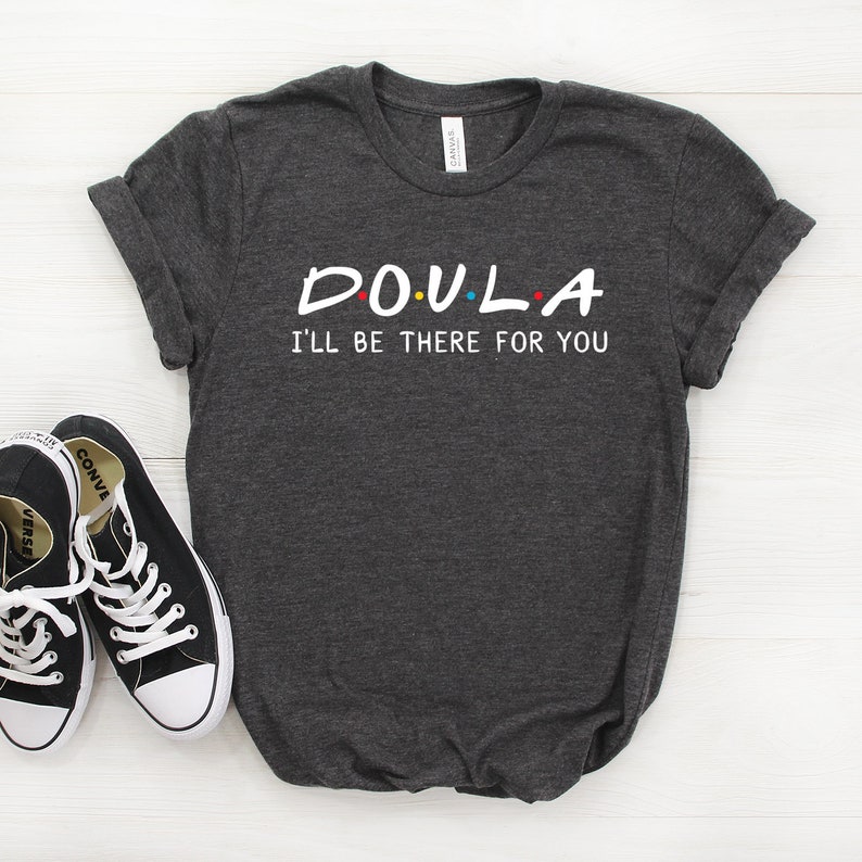 May include: A dark gray t-shirt with the text "DOULA I'LL BE THERE FOR YOU" in white. The letters in "DOULA" are in different colors.