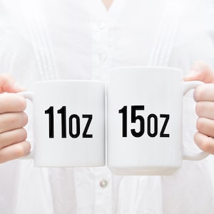 K&ouml;nnte beinhalten: Zwei wei&szlig;e Keramikbecher mit schwarzem Text. Der Becher links zeigt "11oz" und der Becher rechts zeigt "15oz".