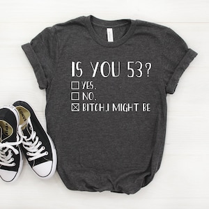 May include: A dark grey t-shirt with the text "IS YOU 53?" and a checkbox list with the options "YES", "NO", and "BITCH, I MIGHT BE". The checkbox next to "BITCH, I MIGHT BE" is checked.
