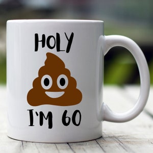 May include: White ceramic coffee mug with a brown poop emoji and the text "HOLY I'M 60" printed on it.