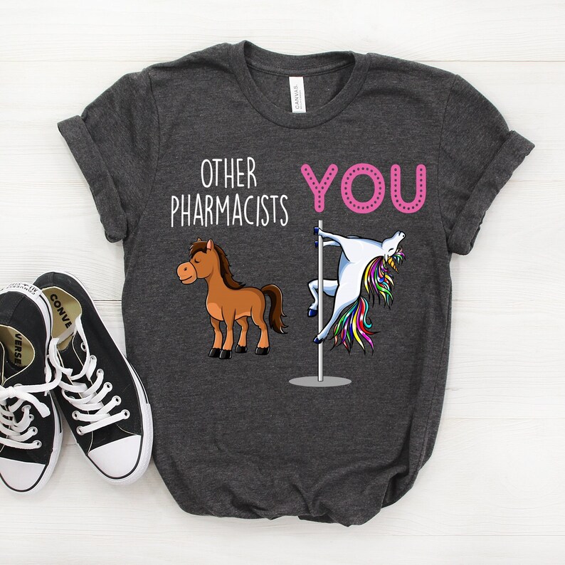 May include: A dark gray t-shirt with the text "Other Pharmacists" and "You" in pink. The text is accompanied by a cartoon horse and a unicorn on a pole.