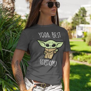 May include: A dark gray t-shirt with a white graphic of a green cartoon character with the text "YODA BEST (CUSTOM)"