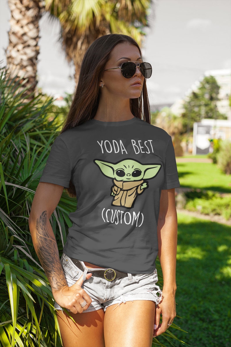 May include: A dark gray t-shirt with a white graphic of a green cartoon character with the text "YODA BEST (CUSTOM)"