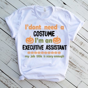 May include: White t-shirt with the text "I don't need a costume I'm an Executive Assistant my job title is scary enough" and a pumpkin graphic.