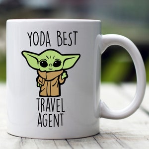 May include: White ceramic mug with a green cartoon character and the text "YODA BEST TRAVEL AGENT".