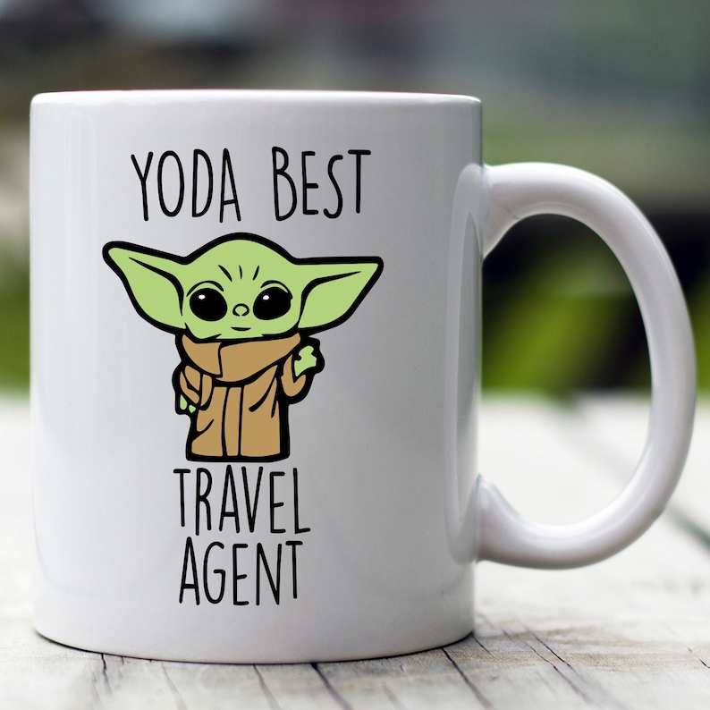 May include: White ceramic mug with a green cartoon character and the text "YODA BEST TRAVEL AGENT".