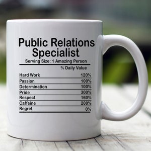 May include: White ceramic mug with a black graphic that reads "Public Relations Specialist" and a nutrition facts label listing "Hard Work", "Passion", "Determination", "Pride", "Respect", "Caffeine", and "Regret" with percentages next to each item.