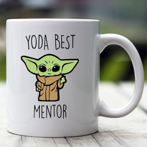 Op de afbeelding: Witte keramische mok met een groen cartoonfiguur van Baby Yoda, de tekst "YODA BEST MENTOR" staat op de mok gedrukt.