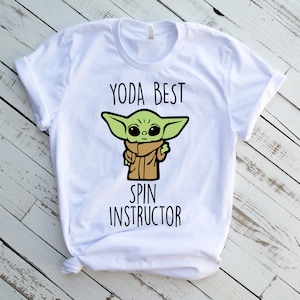 K&ouml;nnte beinhalten: Wei&szlig;es T-Shirt mit einer gr&uuml;nen Comicfigur und dem Text "Yoda Best Spin Instructor".
