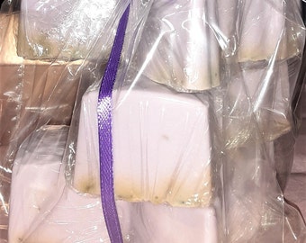 May include: A stack of four lavender-coloured soap bars wrapped in clear plastic with a purple ribbon.