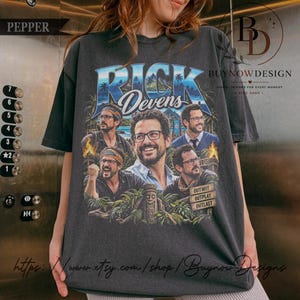 Könnte beinhalten: Ein anthrazitfarbenes Kurzarm-T-Shirt mit einem Grafikdruck von Rick Devens. Das Design zeigt mehrere Porträts des Mannes, einen tropischen Inselhintergrund, eine Tiki-Statue und den Text "RICK Devens" mit "OUTWIT OUTPLAY OUTLAST".