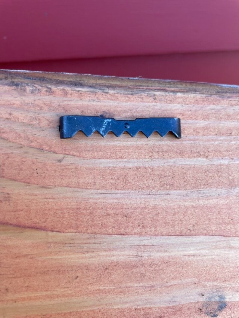 May include: A close-up of a black metal sawtooth hanger attached to the back of a wooden sign.