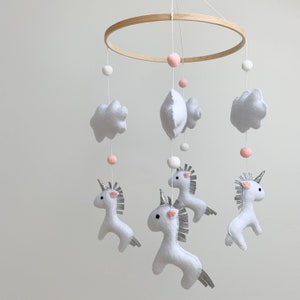 Könnte beinhalten: Ein weißes und silbernes Einhorn-Babymobil mit Wolken und Bommeln, die an einem Holzreifen hängen.