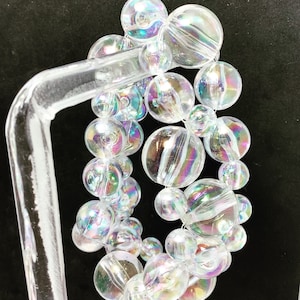 May include: A close-up of an iridescent glass bead bracelet. The beads are round and have a rainbow effect. The bracelet is on a clear plastic stand.