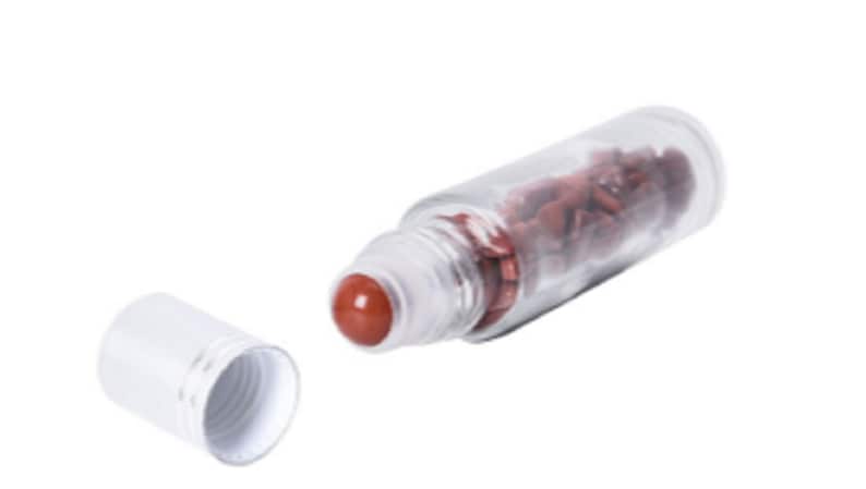May include: A clear glass roller bottle with a white cap and a red roller ball. The bottle is filled with small, red, irregularly shaped stones.