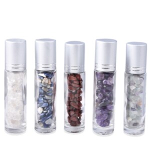 May include: Five clear glass roller bottles with silver caps filled with different colored stones. The bottles are arranged in a row from left to right. The stones are white, blue, red, purple, and green.