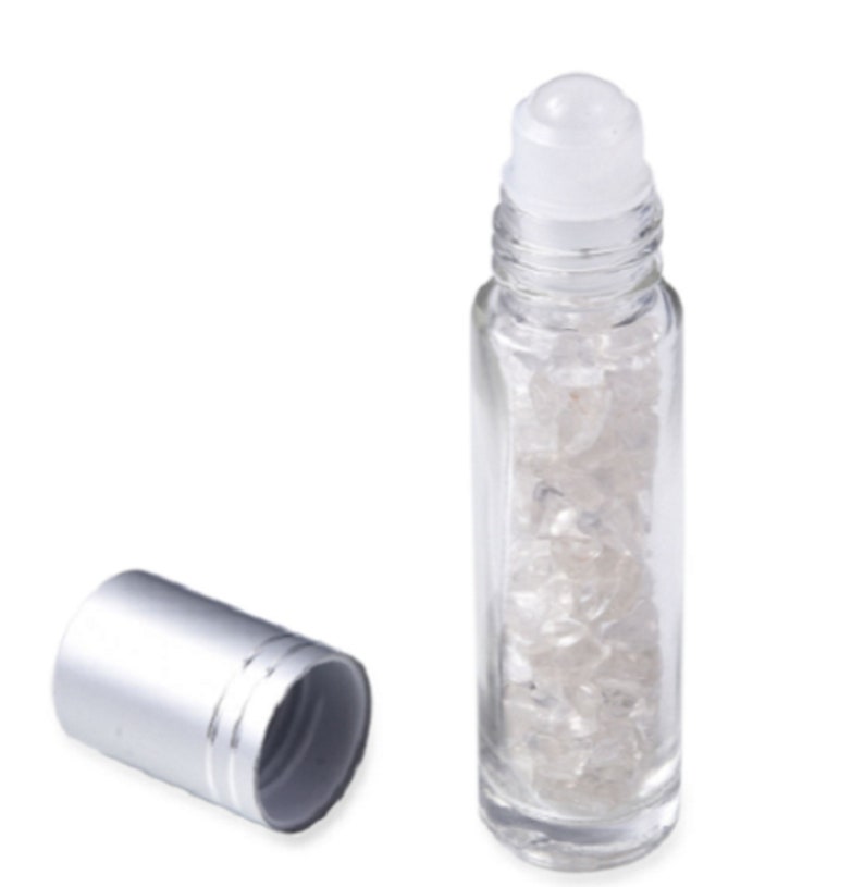 May include: A clear glass roller bottle with a silver cap and a white roller ball. The bottle is filled with small, clear crystals.