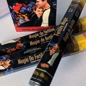 May include: A set of black incense sticks with gold lettering. The packaging features a couple embracing and the text "Fertility Magic", "Magie de fertilité", and "Magia de fertili".