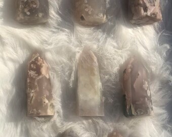May include: Eight grey and white agate crystal points with a pointed top and a flat base. The crystals are arranged in two rows of four on a white fluffy surface.